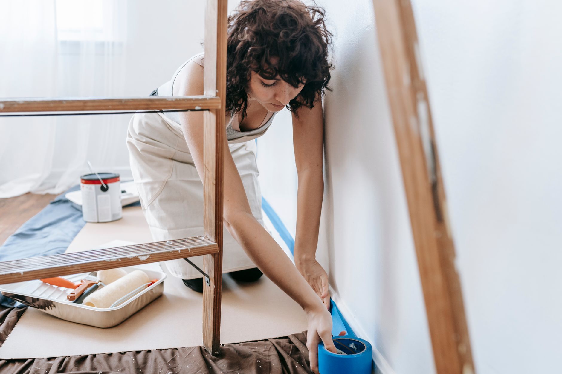 Woman uses tape to prep wall for painting, part of a DIY home renovation project indoors in Pasadena, CA